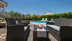 Une terrasse extérieure aménagée avec des meubles en osier, une piscine et une vue sur un bâtiment en arrière-plan.