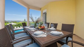 Un coin repas avec une table dressée pour quatre personnes, donnant sur une piscine et un espace verdoyant.