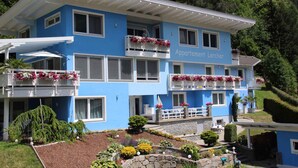 Un edificio azul de dos pisos con balcones decorados con flores, con el letrero "Appartement Lercher".