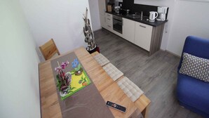 Una cocina compacta con electrodomésticos modernos, una mesa de comedor con control remoto y una silla azul.