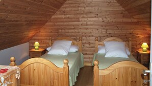 A cozy attic bedroom with two wooden beds, each with a nightstand and a lamp. - 3 bedroom beach front home in Kerbors (Kerbors)