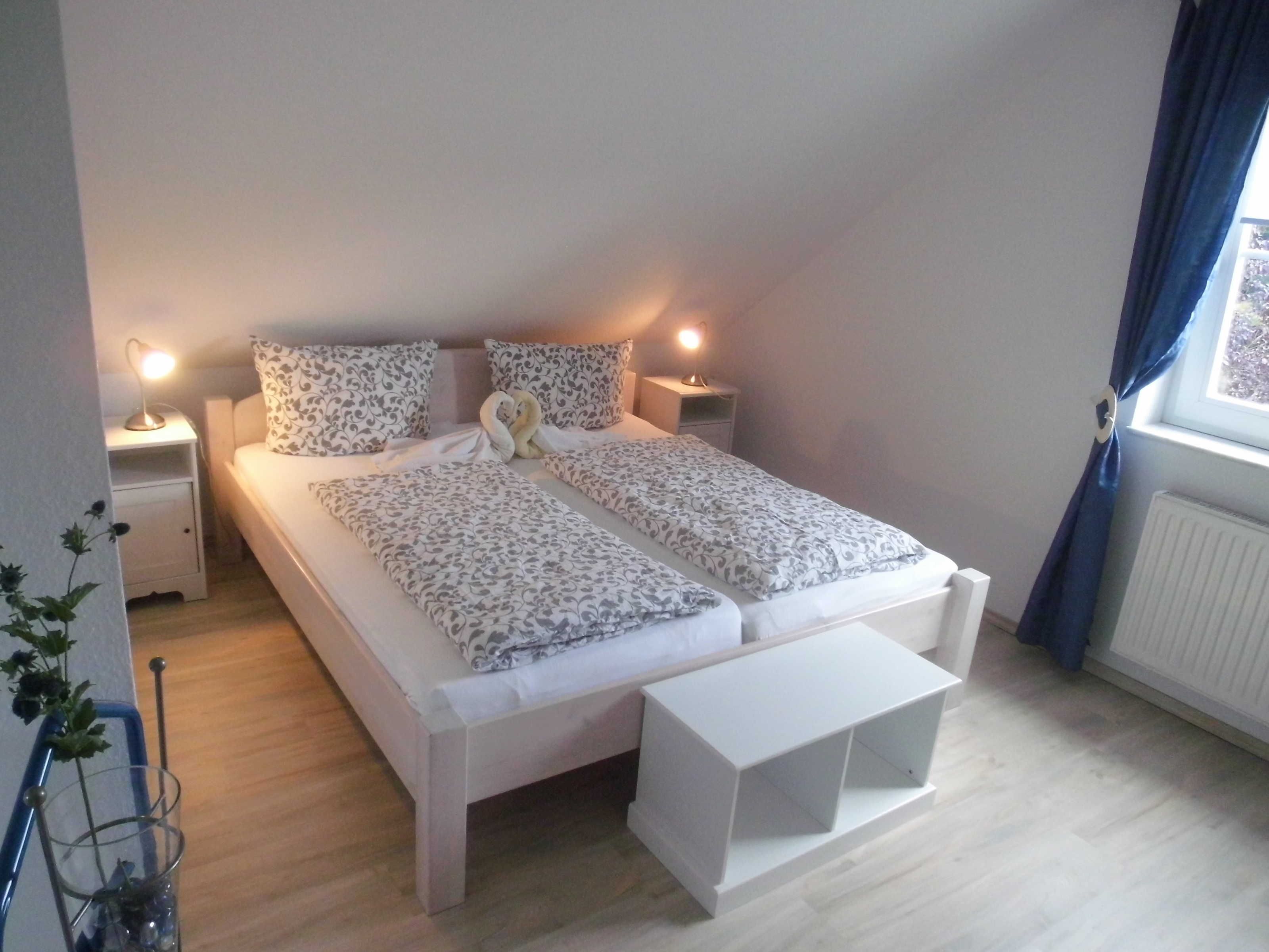 A bedroom with a bed, bedside tables, a bedside lamp, a window with curtains, and a radiator.