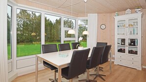 Een eetruimte met een tafel en stoelen, grote ramen, een klok en een kast met glazen deuren.