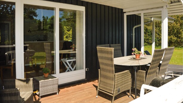 Een overdekt terras met rieten meubilair, een tafel en stoelen, en een schuifdeur naar een tuin.