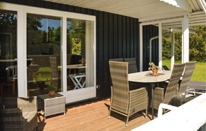 Une terrasse couverte, aménagée avec des meubles en osier, une table et des chaises, et une porte-fenêtre coulissante donnant sur un jardin.