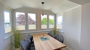 A dining area with a wooden table, six chairs, a hanging light fixture, and large windows with blinds. - Villa Störtebeker Whg. 08 - Villa Störtebeker Whg. 08 (Göhren)