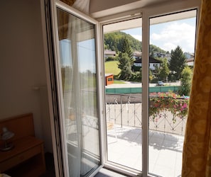 Una habitación con puerta de vidrio corredera que da a un balcón con vistas a casas y vegetación.