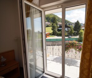 Ein Zimmer mit einer Schiebeglastür, die auf einen Balkon mit Blick auf Häuser und Grünflächen führt.