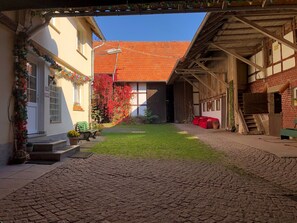 Ein Innenhof mit einem Kopfsteinpflasterweg, einem Gebäude mit rotem Dach und einer Holzkonstruktion mit Treppe.