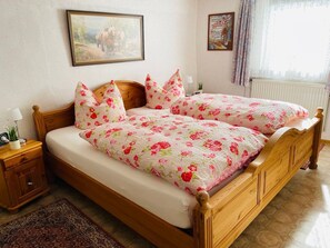 Ein Doppelbett mit floralem Bettbezug, ein Holz-Kopfbrett, ein Nachttisch mit Lampe und eine kleine Pflanze.