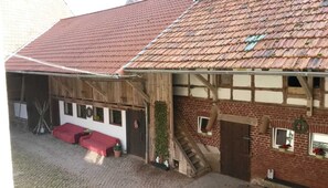 Ein traditionelles Fachwerkhäuschen mit einem geneigten, rot gedeckten Dach, einer Holztreppe und einer überdachten Außenbereich-Sitzgelegenheit.