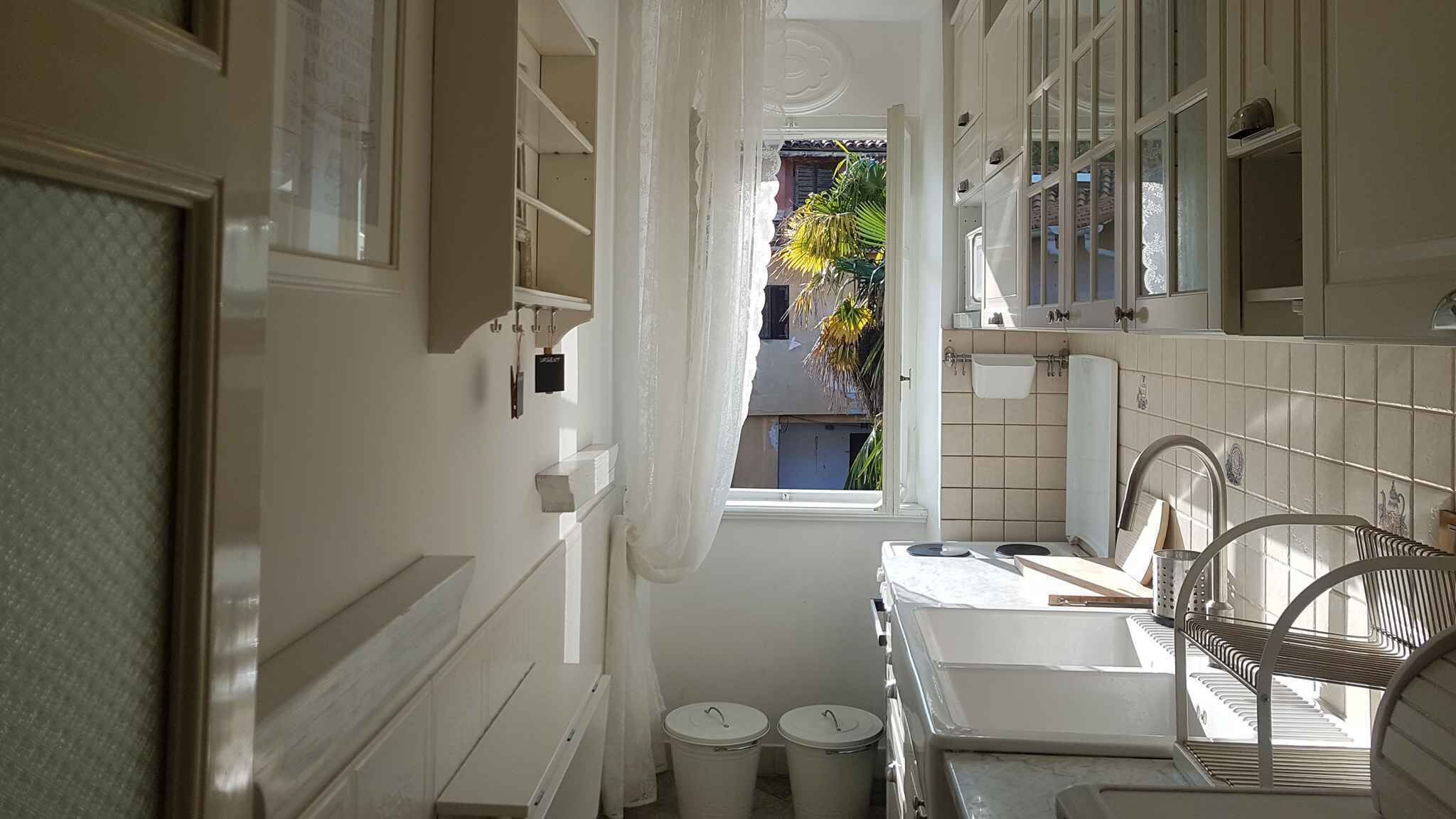 Un bagno stretto con una finestra, sanitari bianchi e vista su un edificio.