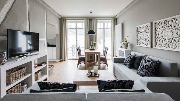 Ein modernes Wohnzimmer mit Flachbildfernseher, grauem Sofa und einem Essbereich mit Tisch und Stühlen.