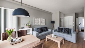 Ein modernes Wohnzimmer mit zwei grauen Sofas, einem Holztisch, einem Esstisch mit Stühlen und einer schwarzen Pendelleuchte.