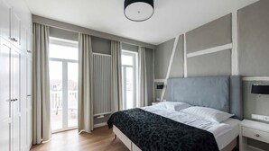 Ein modernes Schlafzimmer mit einem großen Bett, einem Nachttisch, einem Fernseher und Blick auf die Stadt durch das Fenster.