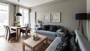 Ein modernes Wohnzimmer mit grauem Sofa, einem Holztisch, einem Essbereich mit Tisch und Stühlen sowie dekorativer Wandgestaltung.