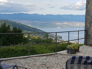 A balcony with a view of a coastal city, a stone wall, and a potted plant.