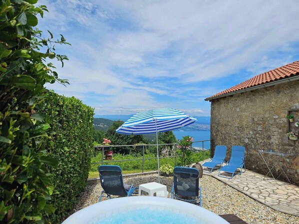 Relax in a serene outdoor setting with a clear view of the water, featuring a hot tub and lounge chairs amidst lush greenery.