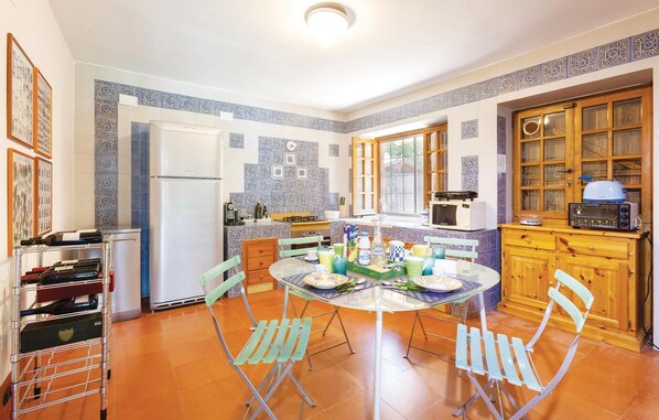 A compact kitchen with a round dining table, green folding chairs, a refrigerator, a microwave, and wooden cabinets. - Nice home in Contursi Terme (SA) with sauna (Contursi Terme (SA))