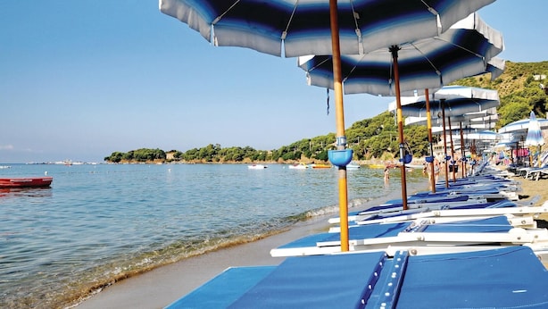 A beach with rows of sun loungers and umbrellas, a calm sea, and a distant shoreline with buildings and greenery. - Nice home in Contursi Terme (SA) with sauna (Contursi Terme (SA))