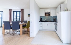 A modern kitchen with white cabinets, a black countertop, and stainless steel appliances. There is a dining area with a wooden table and chairs.