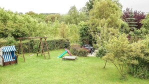 A backyard with a swing set, a slide, and a blue-striped chair. - Apartment with Jacuzzi (5) - Apartment near the beach (Nienhagen)