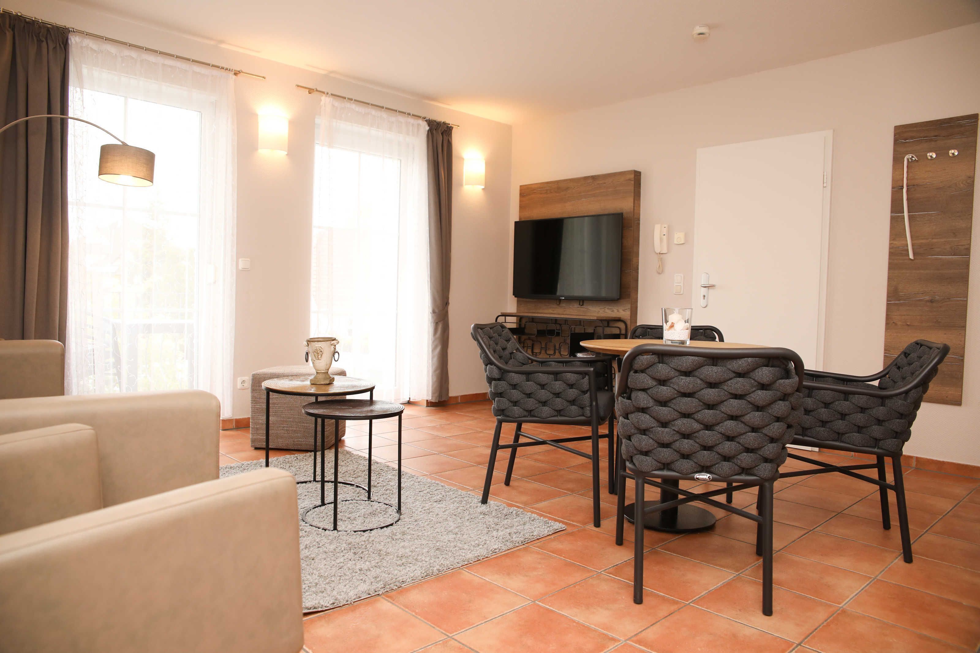 Uma sala de estar moderna com um sofá, uma mesa de jantar com cadeiras, uma TV na parede e uma janela com cortinas.