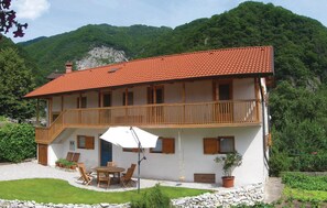 Un edificio a due piani con tetto in tegole rosse, balconi in legno e un patio con tavolo e sedie.
