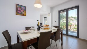 Un espace repas avec une table blanche, des chaises marron, un lustre et une vue sur la ville à travers de grandes fenêtres.