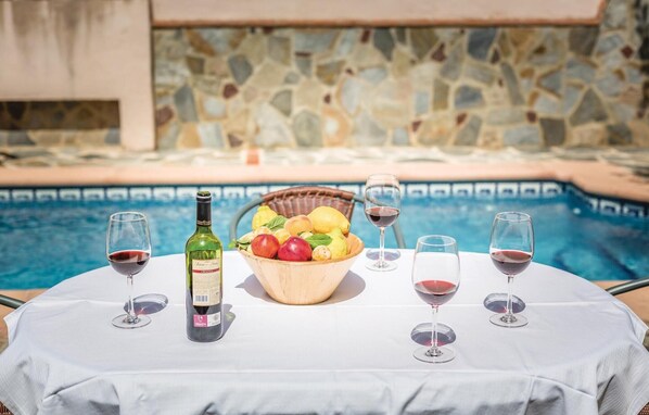 A poolside table with a bottle of wine, a bowl of fruit, and wine glasses. - Stunning home in Montecorto, Málaga (Montecorto, Málaga)