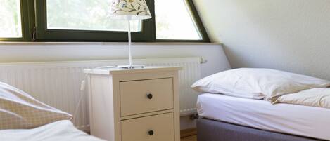 A bedroom with a bed, a bedside table with a lamp, a radiator, and a window.