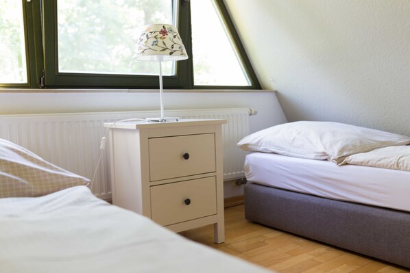 Un dormitorio con una cama, una mesita de noche con lámpara, un radiador y una ventana.