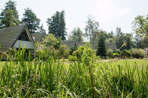 A row of modern, triangular-roofed buildings with a well-maintained lawn and dense greenery in the foreground.