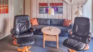 Een kamer met een bank, twee leren fauteuils, een ronde houten tafel en een schilderij aan de muur.