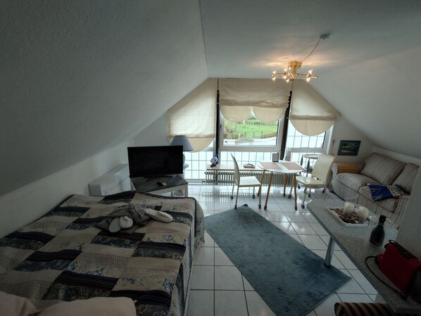 Een slaapkamer met een bed, televisie, bureau, stoel, bank en uitzicht op het omliggende landschap.