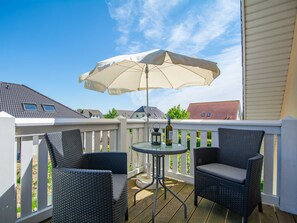 A balcony with wicker chairs, a table, and a large umbrella.
