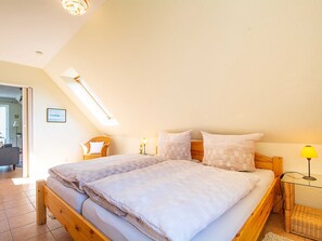 A bedroom with a wooden bed, a skylight, a small table with a lamp, and a chair.