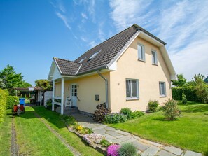 A two-story house with a sloped roof, a covered porch, and a well-maintained garden with a stone pathway.