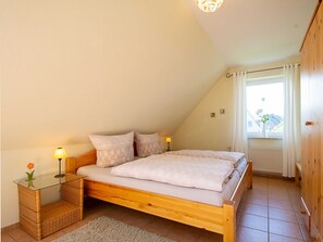 A bedroom with a wooden bed, two bedside tables with lamps, a small rug, and a window with curtains. - Meadow ground 18 Whg. WiGr-18 - meadow ground 18 (Kühlungsborn)