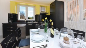 A modern kitchen with black cabinets, a dining area with a white table set for two, and a view of the outdoors through the windows. - Amazing home in Lecevica (Lecevica)