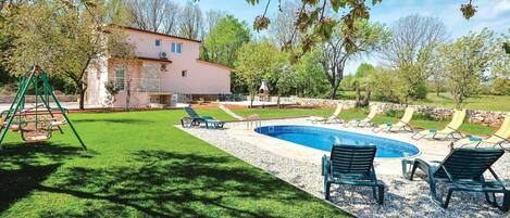A backyard with a swimming pool, lounge chairs, and a swing set.