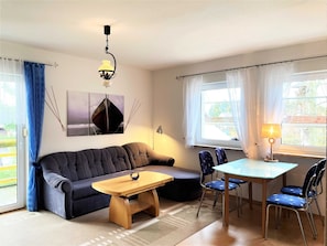 Een gezellige woonkamer met een bank, een houten salontafel, een eettafel met stoelen, een lamp en een schilderij aan de muur.