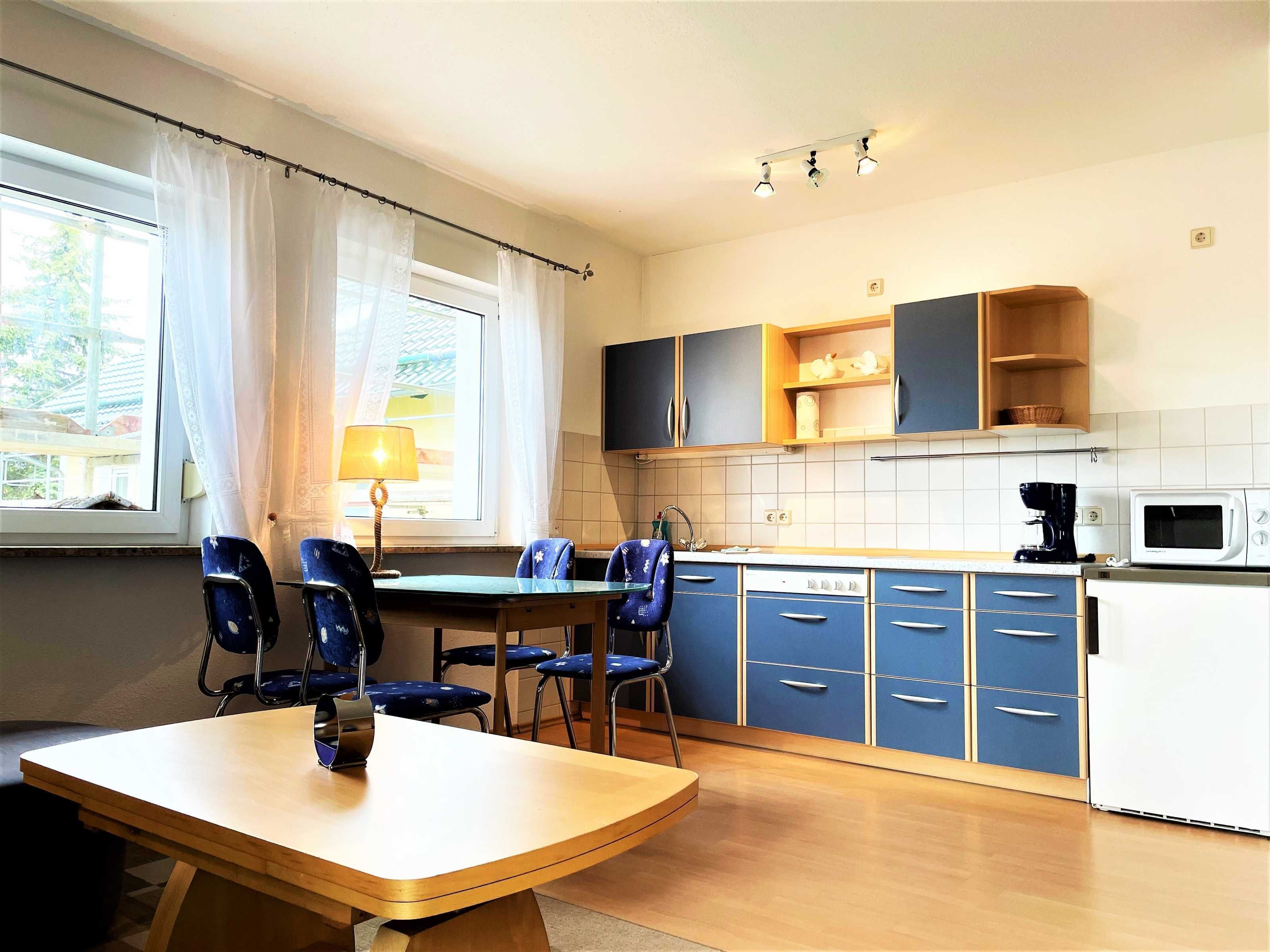 A kitchen with blue cabinets, a dining table with chairs, a window with curtains, and a microwave.