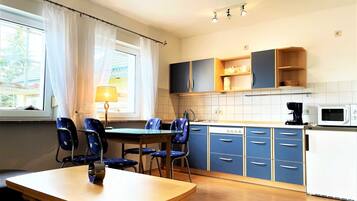 A kitchen with blue cabinets, a dining table with chairs, a window with curtains, and a microwave.