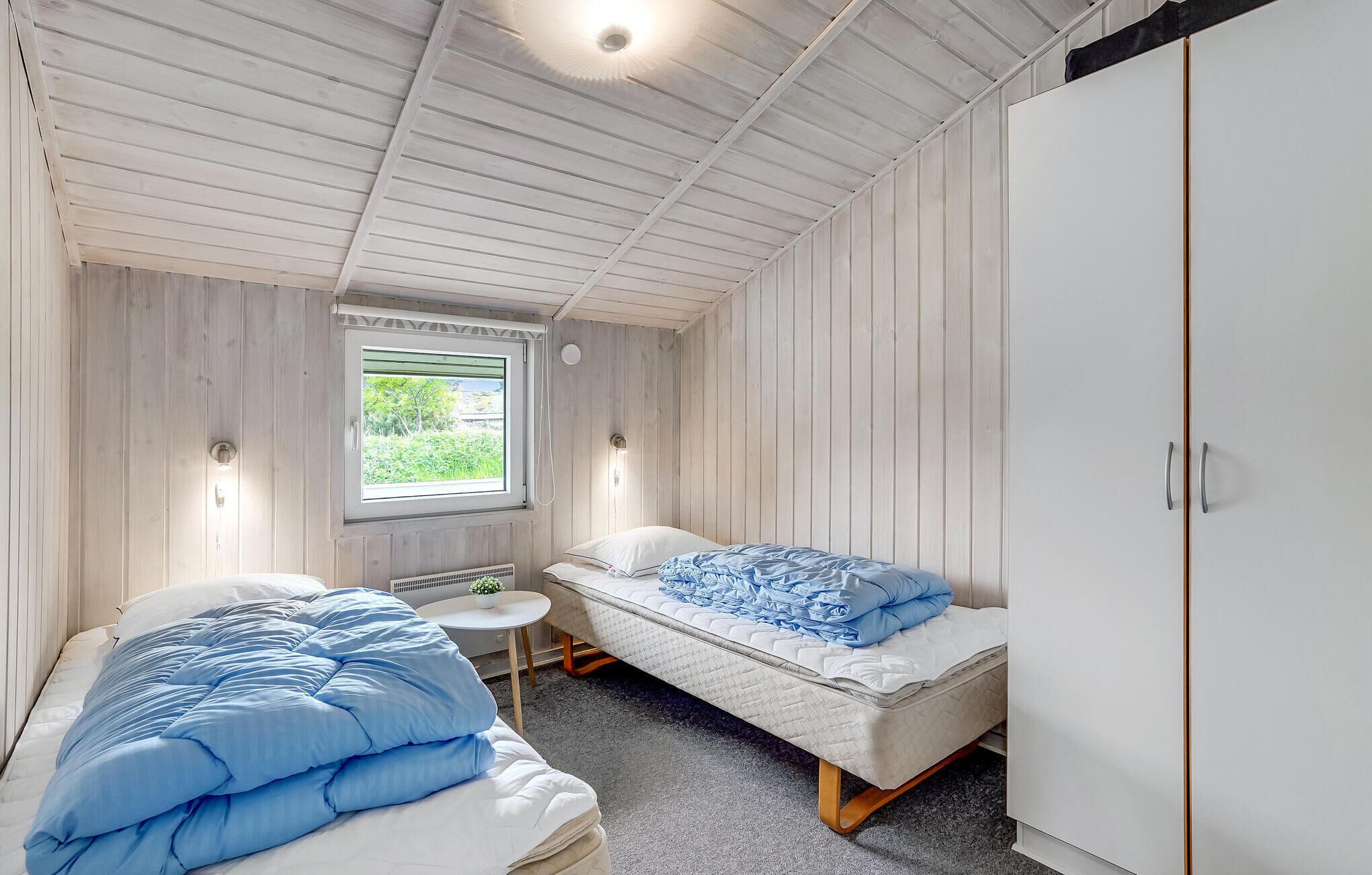 A small, cozy room with two beds, a window, and a wardrobe.