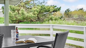 Un espacio de estar al aire libre techado con una mesa, una silla, un libro y una botella de cerveza.