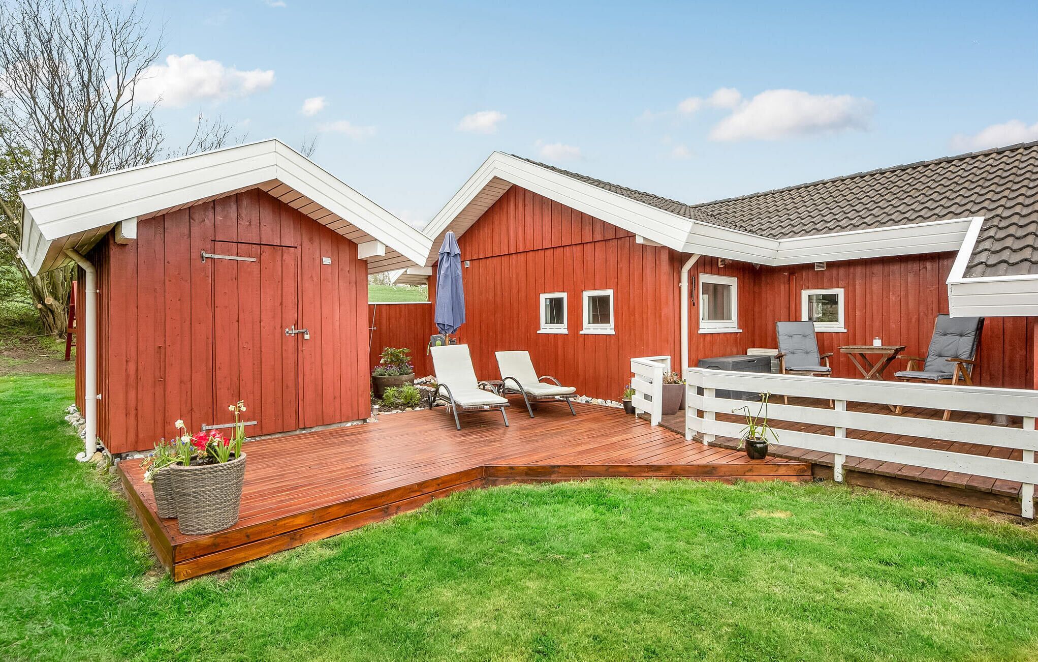 Een rode houten constructie met terras en zitgedeelte buiten.