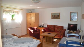 A cozy living room with a bed, two armchairs, a sofa, a wooden cabinet, a television, and a table. - Bebensee, DZ DU / WC - Bebensee, Edda DZ (Neustadt in Holstein)