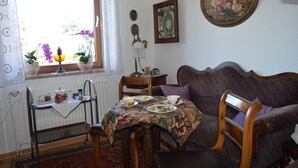 A dining area with a table set for two, a sofa, a radiator, and a window with curtains. - Bebensee, DZ DU / WC - Bebensee, Edda DZ (Neustadt in Holstein)