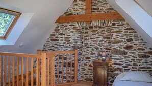 A bedroom with a stone wall, wooden ceiling beams, a wooden crib, a bedside table with a lamp, and a bed. - Amazing home in Minihy Treguier (Minihy Treguier)